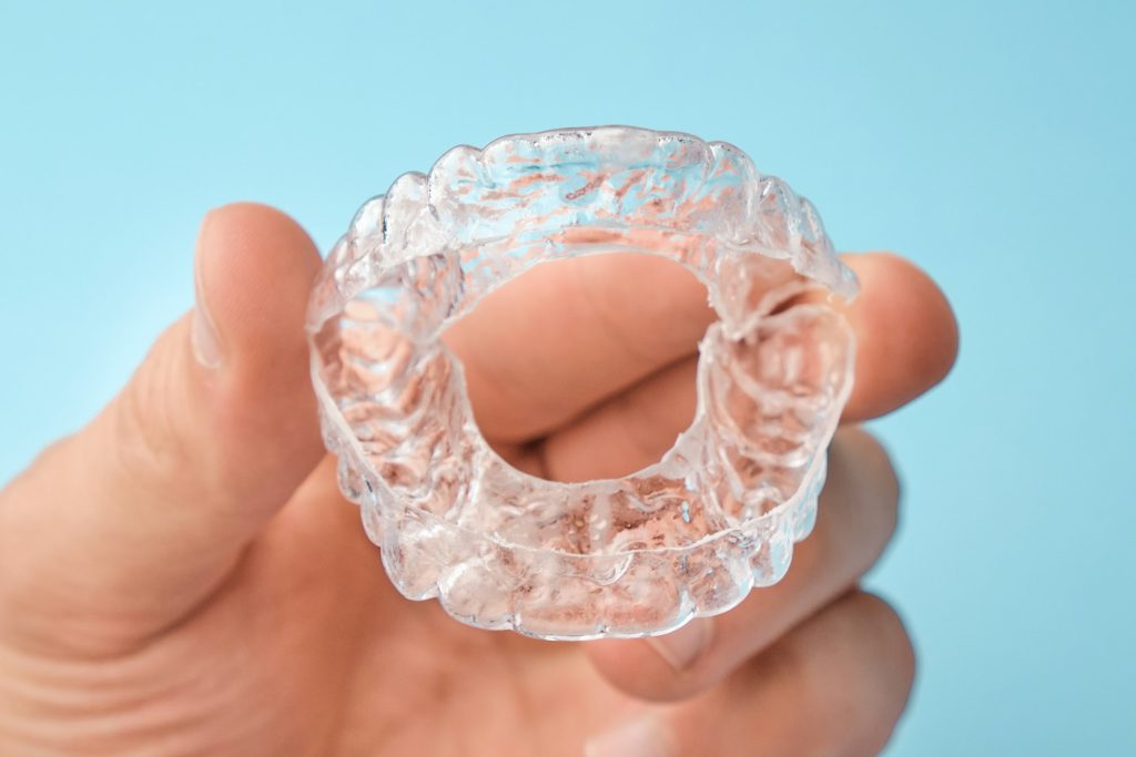 Close up mans hand holding invisible aligners for whitening and straightening of teeth on the blue