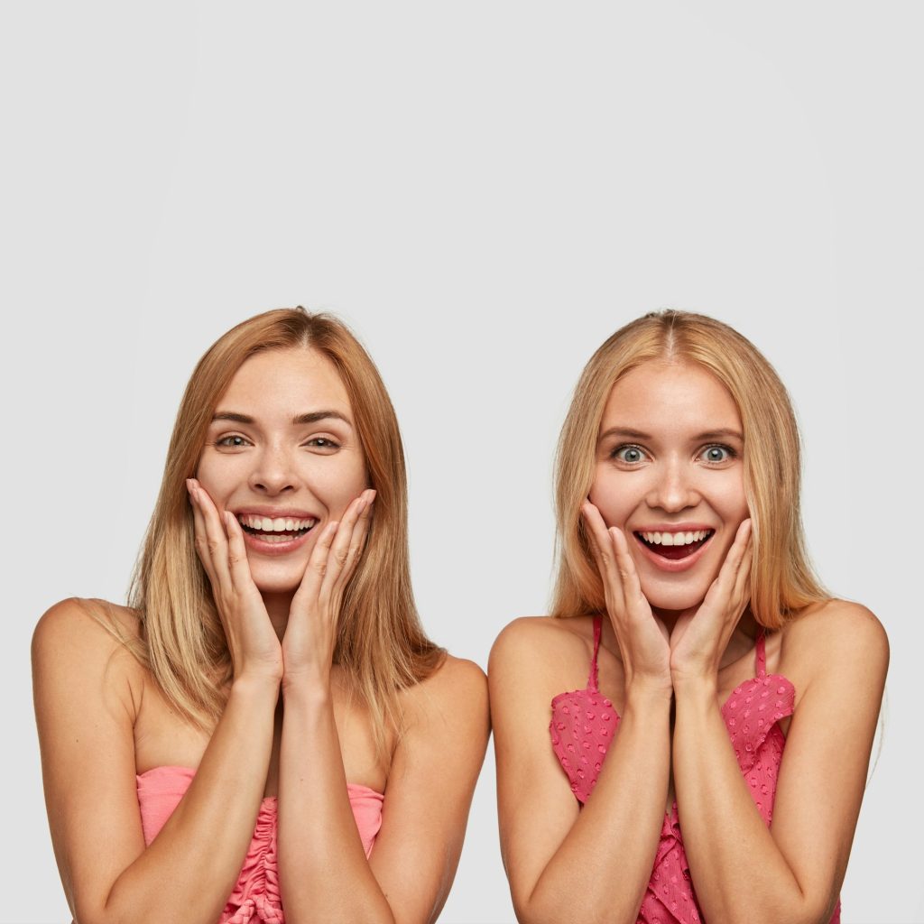 Vertical portrait of joyful two girls with broad smiles, being amazed as see something incredible an